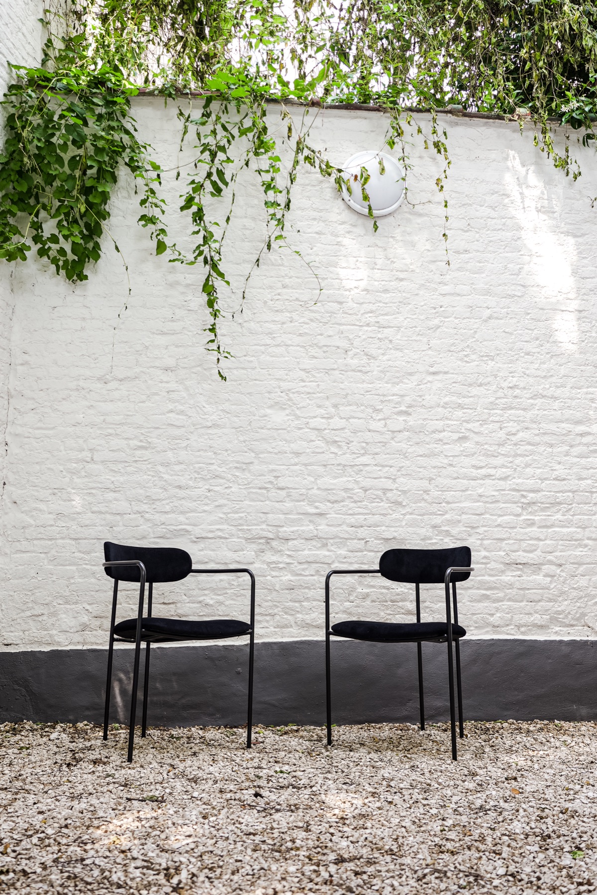 Two black chairs against a white brick courtyard wall at RAIBU